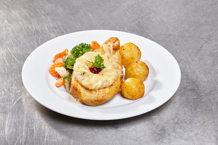 A beautifully arranged plate features roasted chicken topped with a creamy sauce, accompanied by vibrant vegetables and crispy potato balls. The warm lighting adds to the inviting atmosphereの写真素材