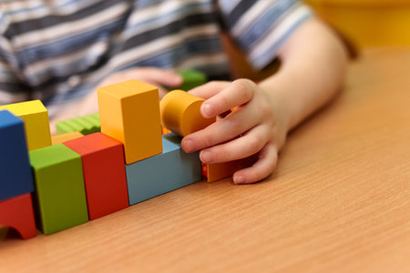 A young child is actively engaged in stacking colorful wooden blocks on a table, displaying creativity and focus in a cheerful indoor environmentの写真素材