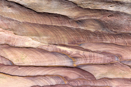 Detailed view of layered sandstone rock formations in Wadi Ghuweir, Jordan. Natural wavy patterns reveal geological history with rich earth tones and smooth surfaces shaped by water and wind erosionの写真素材