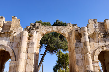 Ancient stone arches stand tall in Jerash, Jordan, highlighting the remarkable remnants of Greco-Roman architecture. Lush greenery surrounds the ruins, creating a serene atmosphere.の写真素材