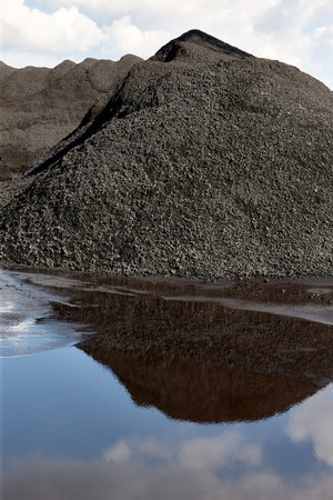 A significant pile of coal is situated at an industrial location, with its glossy surface mirrored...