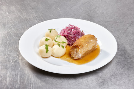 A well-prepared dish featuring tender chicken breast with a rich sauce, potato dumplings, and a serving of pickled red cabbage garnished with fresh herbsの写真素材
