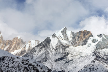 Mountains covered in snow and glacier stretch towards the sky in the Himalayas. Wisps of clouds surround the peaks, viewed from the Annapurna Base Camp trek in Nepal.の写真素材