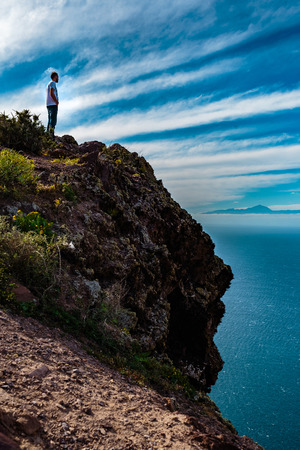 man standing on a hill above the ocean, an island in the background and blue skyの写真素材