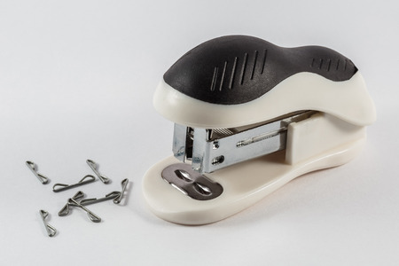 white and black stapler with staples lying next to a white backgroundの写真素材