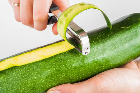 Peeling zucchini with peeler on white background
