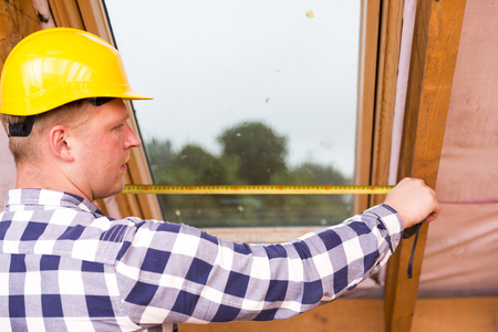 Handyman in safety helmet measuring roof window, attic renovationの写真素材