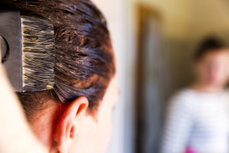 Woman with dying her hair in front of mirror in her own bathroom.の写真素材