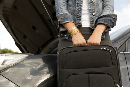 Young woman with suitcase next to the broken car ready to leave itの写真素材