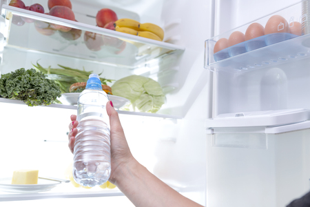 Woman taking a water bottle out of the fridgeの写真素材