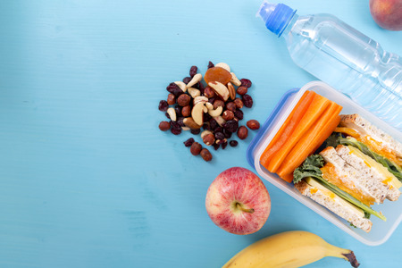 School lunch box with sandwich, vegetables, water, nuts and fruits on turquoise background. Healthy eating habits conceptの写真素材