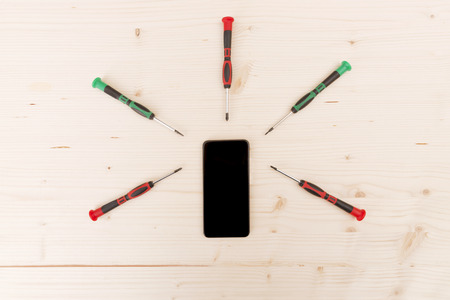 Mobile phone repair. Phone with screwdrivers around on wooden backgroundの写真素材