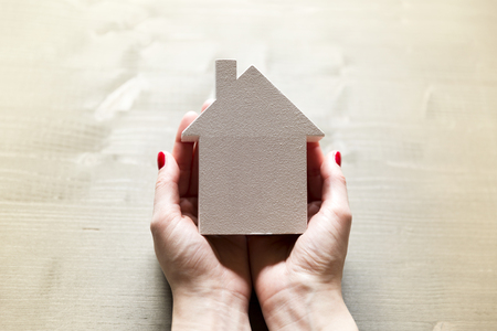 Woman holding in hands small white model house as a sign of protection, insurance and importance of own homeの写真素材