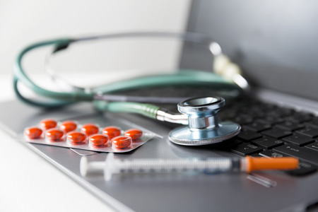 Pack of medicine pills, syringe and stethoscope laying on laptop keyboard. Medicine industry conceptの写真素材