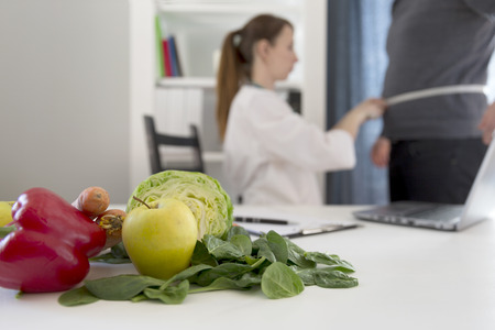 Vegetable diet nutrition and medication concept. Nutritionist measures patient's waist and offers healthy vegetables diet.の写真素材