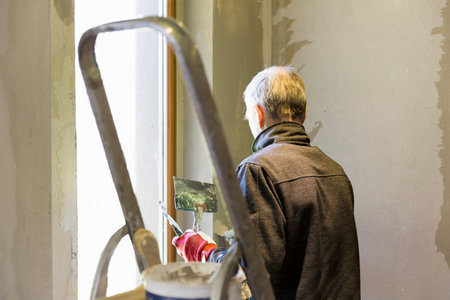 Plasterer home improvement handyman worker with putty knife working on apartment wall filling. Home...