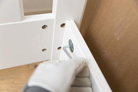 Assembling new wooden bed by hand in room. Man putting together new furniture.の写真素材