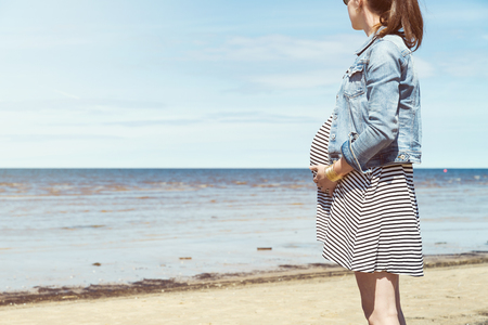 Beautiful pregnant woman standing on the beach. Pregnant woman taking a walk by the beachの写真素材