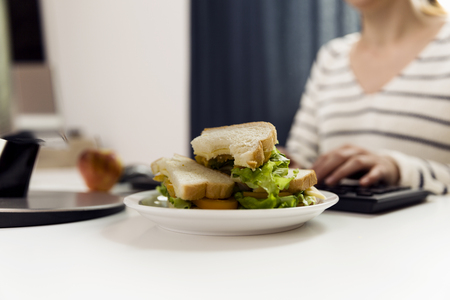 Woman eating sandwich while working. Sandwich from fresh toast with cheese and salad on work place. Work lunchの写真素材