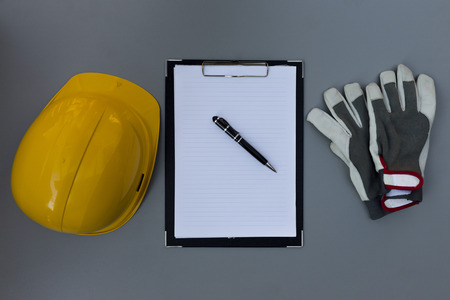 Yellow helmet, hard hat, notebook, pen and gloves on grey table. Construction plan conceptの写真素材