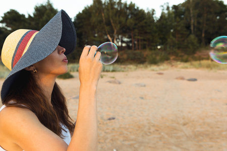 Woman portrait blowing soap bubbles at the beach. Beautiful sunset