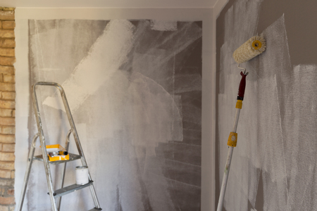 Tools for coloring, paint roller, brush, aluminium leader. Wall partly colored. With focus on paint roller.の写真素材