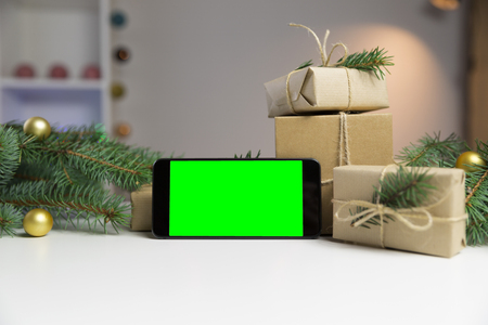 Smart phone with green screen surrounded by Christmas decorations. Holiday and christmas concept. Wrapped christmas gifts.の写真素材
