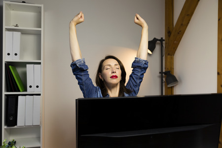 Woman stretching her arms sitting by the table at work next to computer. Working late conceptの写真素材