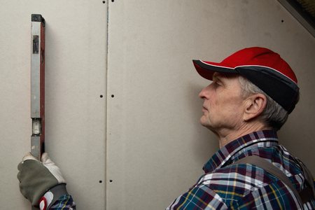 Man holding level against interior drywall. Attic insulation and renovationの写真素材
