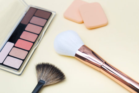 Decorative cosmetics, makeup products and brushes on light pink background