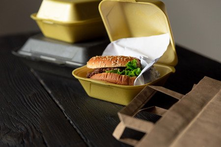 Hamburger in a takeaway container on the wooden background. Food delivery and fast food conceptの写真素材