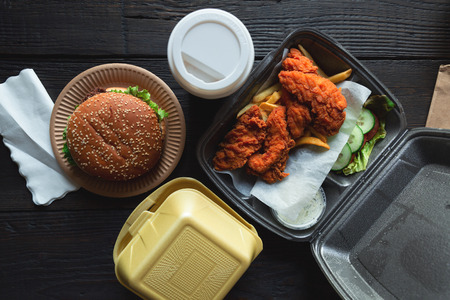 Hamburger, french fries and fried chicken in takeaway containers on the wooden background. Food delivery and fast food concept