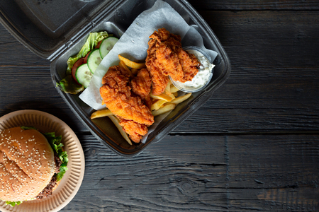 Hamburger, french fries and fried chicken in takeaway containers on the wooden background. Food delivery and fast food conceptの写真素材