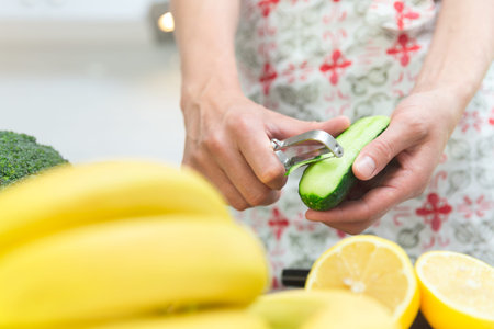 Woman cooking healthy food in her kitchen, she is peeling a fresh cucumber on the chopping board