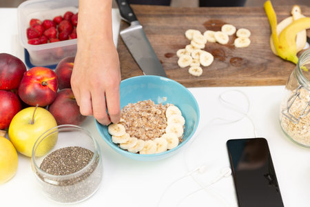 Woman preparing healthy fitness breakfast: oatmeal with bananas, strawberries and chia seeds