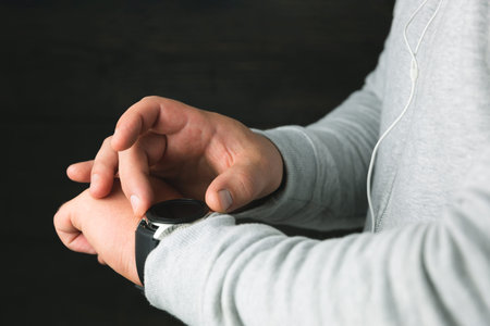 Man in a sport hoodie checking notification on digital smartwatch display. Man's hands with wearable...