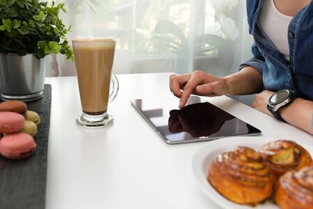 Woman with smartwatch using tablet in coffee shop. Coffee and pastry, macaroons on white table. Freelance workingの写真素材