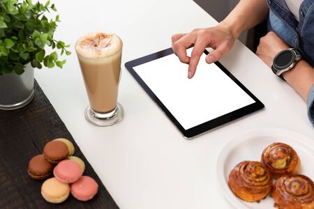 Woman with smartwatch using tablet in coffee shop. Coffee and pastry, macaroons on white table. Freelance workingの写真素材