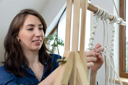 Woman relaxing and making macrame at home with different knots on a sunny day at home in attic. Stay at home hobbies.の写真素材