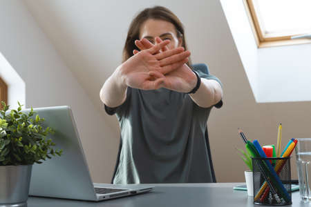 Working from home exercise. Young woman stretching hands while sitting at desk. Healthy living during office hours.の写真素材
