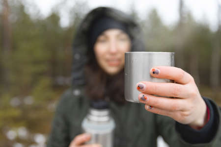 Young women holding a cup of hot beverage with steam during a cold and rainy day. Hiking and healthy living.の写真素材