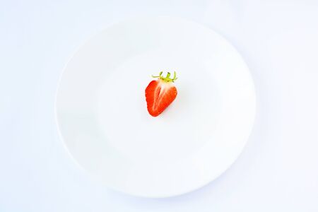 Half ripe strawberries in the center of a white plate, on a white background, minimalismの写真素材