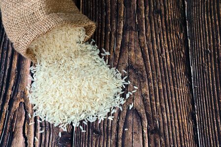 White rice spill out of the burlap bag on the wooden table.の写真素材