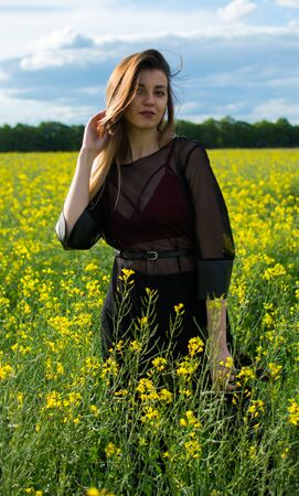Girl in dark clothes with beautiful hair standing in a field of yellow rape. Warm spring dayの写真素材