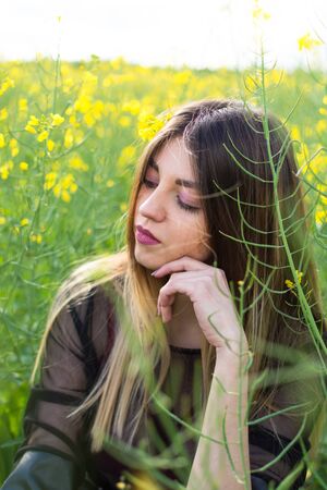 Girl in dark clothes with beautiful hair sitting in a field of yellow rape. Warm spring dayの写真素材
