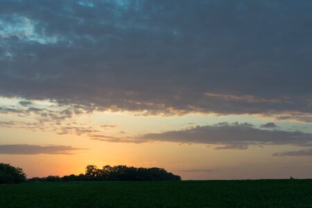 Sunset sunrise over field or meadow. Bright dramatic sky and dark ground. Countryside landscape under scenic colorful sky at sunset dawn sunrise.の写真素材