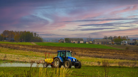A blue tractor sprays fertilizer, with the majestic sky and meadow in the background.