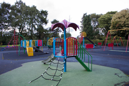 An empty Colourful children playground in the middle of busy park surrounded by the trees. On the...