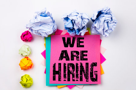 Writing text showing We Are Hiring written on sticky note in office with screw paper balls. Business concept for Recruitment and Job recruiting advertisement on the white background.の写真素材