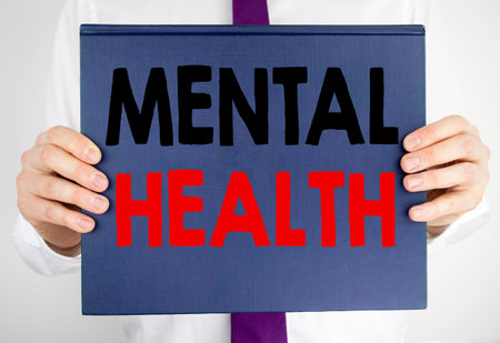 Writing text showing Mental Health. Business concept for Anxiety Illness Disorder written on book notebook paper holding by man in suit blurred background.の写真素材